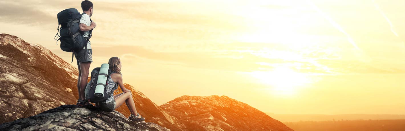 Image of young hiking couple looking at sunrise from mountaintop.